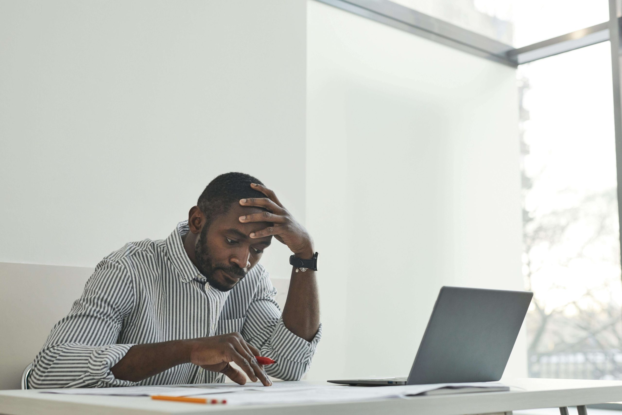 Man sitting at a desk with his laptop, deep in thought and overwhelmed, representing professionals who benefit from psychiatry in Tempe, AZ.