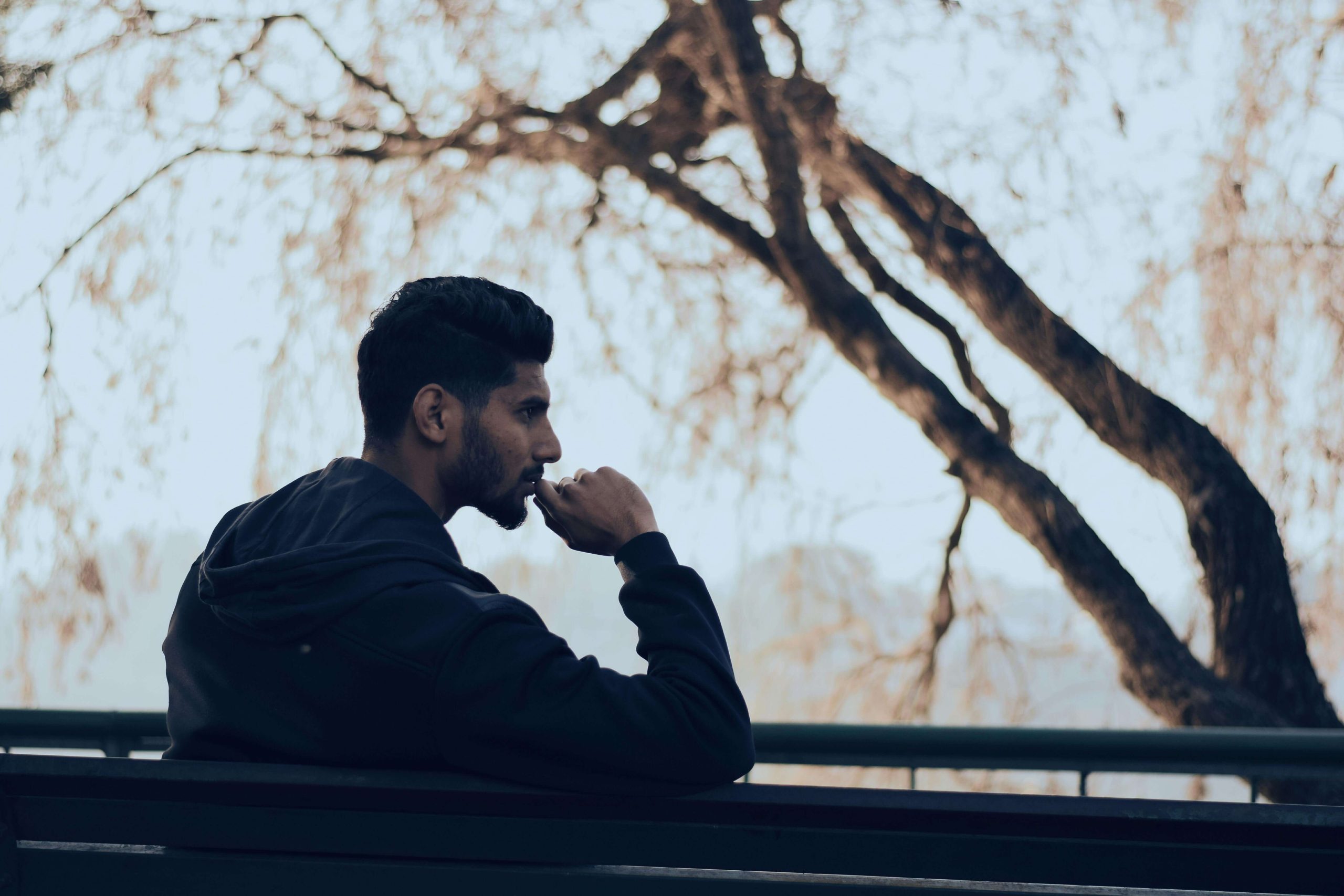 A thoughtful man sitting on a bench under a tree, symbolizing reflection and the journey of mental health recovery supported by ketamine infusion therapy in Tempe, AZ.