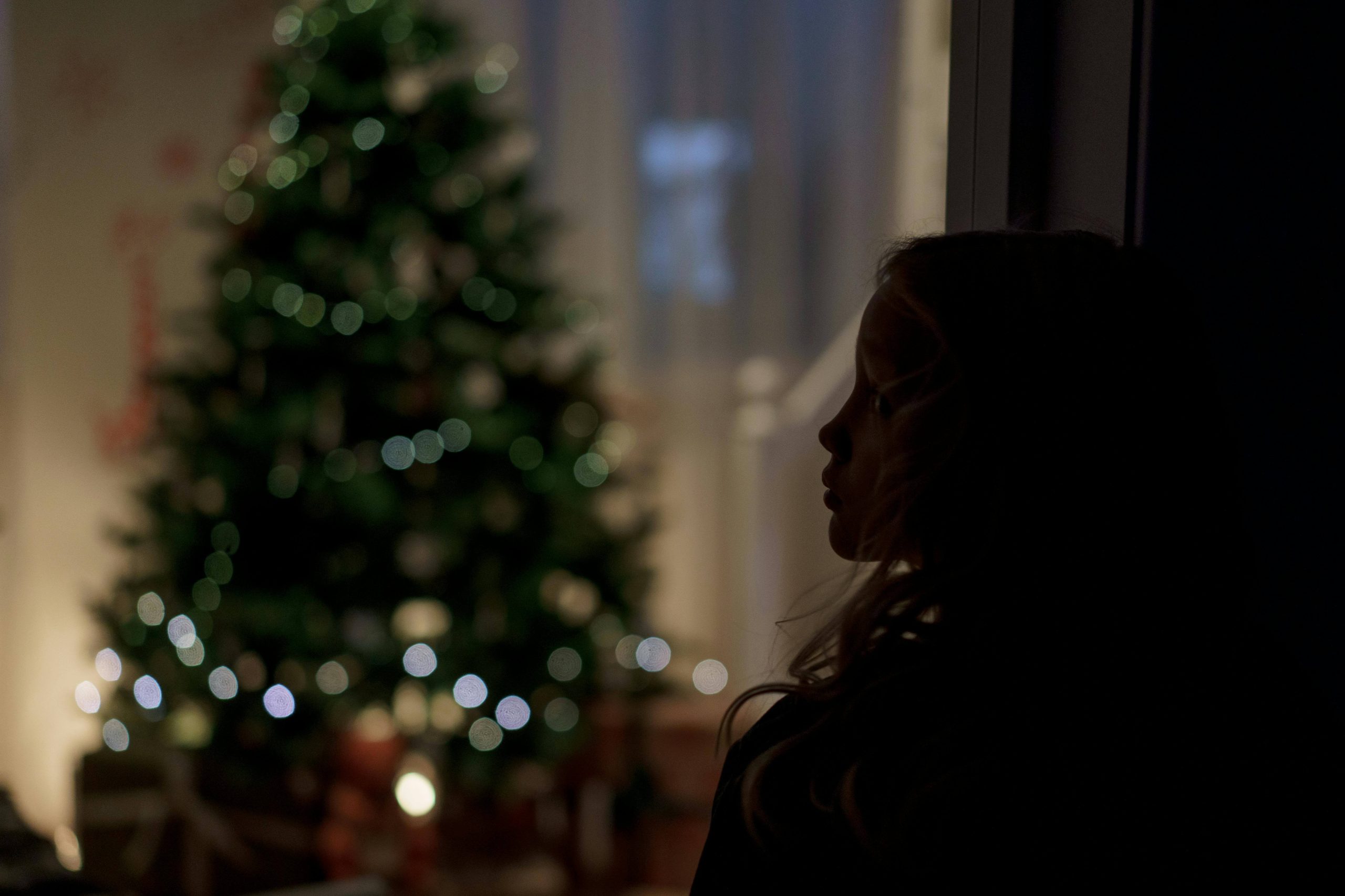 Silhouette of a child gazing at a lit Christmas tree, capturing the quiet loneliness that psychiatry for grief in Tempe, AZ helps families navigate.