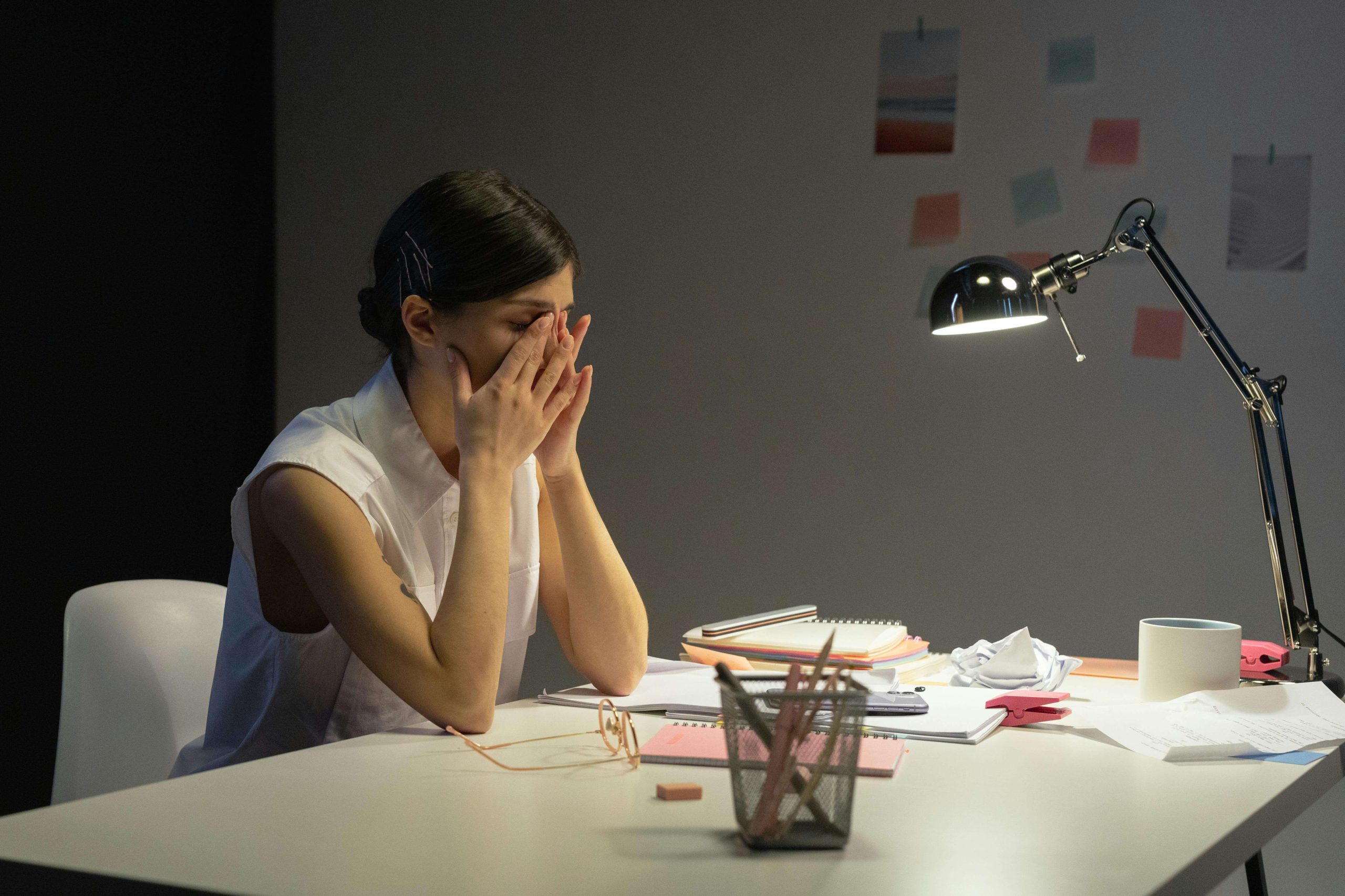 Woman sitting at a desk with her hands covering her face, illustrating the hidden emotional exhaustion high-achievers may face before seeking psychiatry in Tempe, AZ.