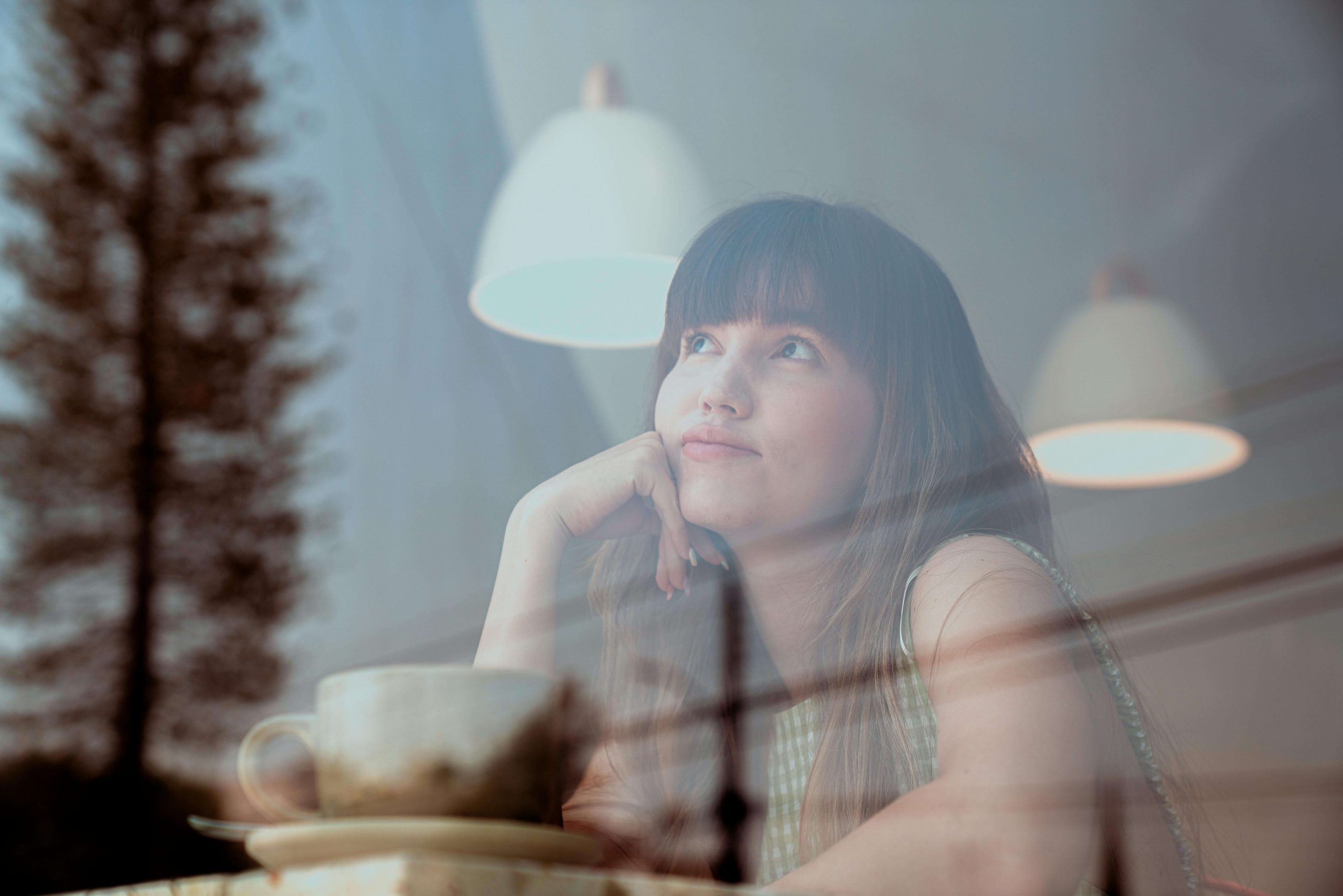 Woman gazing out a café window with a cup of coffee, reflecting on whether ketamine infusion therapy in Tempe, AZ could support her mental health journey.