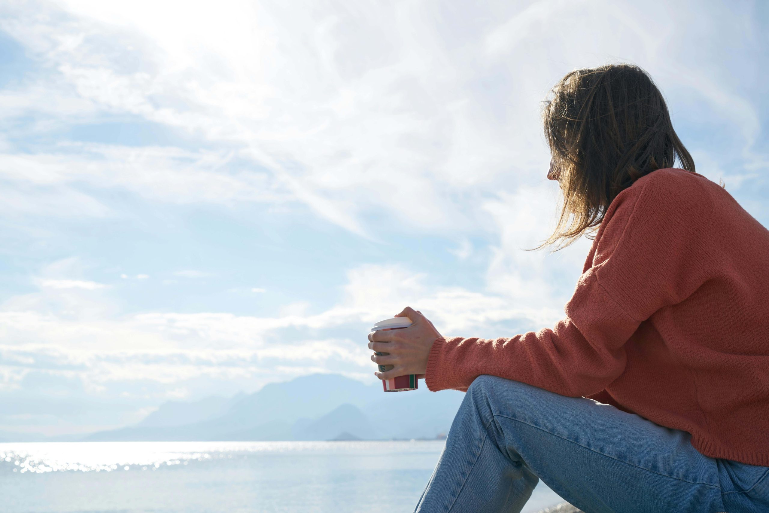 Person sitting by the water holding a cup of coffee, reflecting on life and emotional well-being supported by psychiatry in Tempe, AZ.