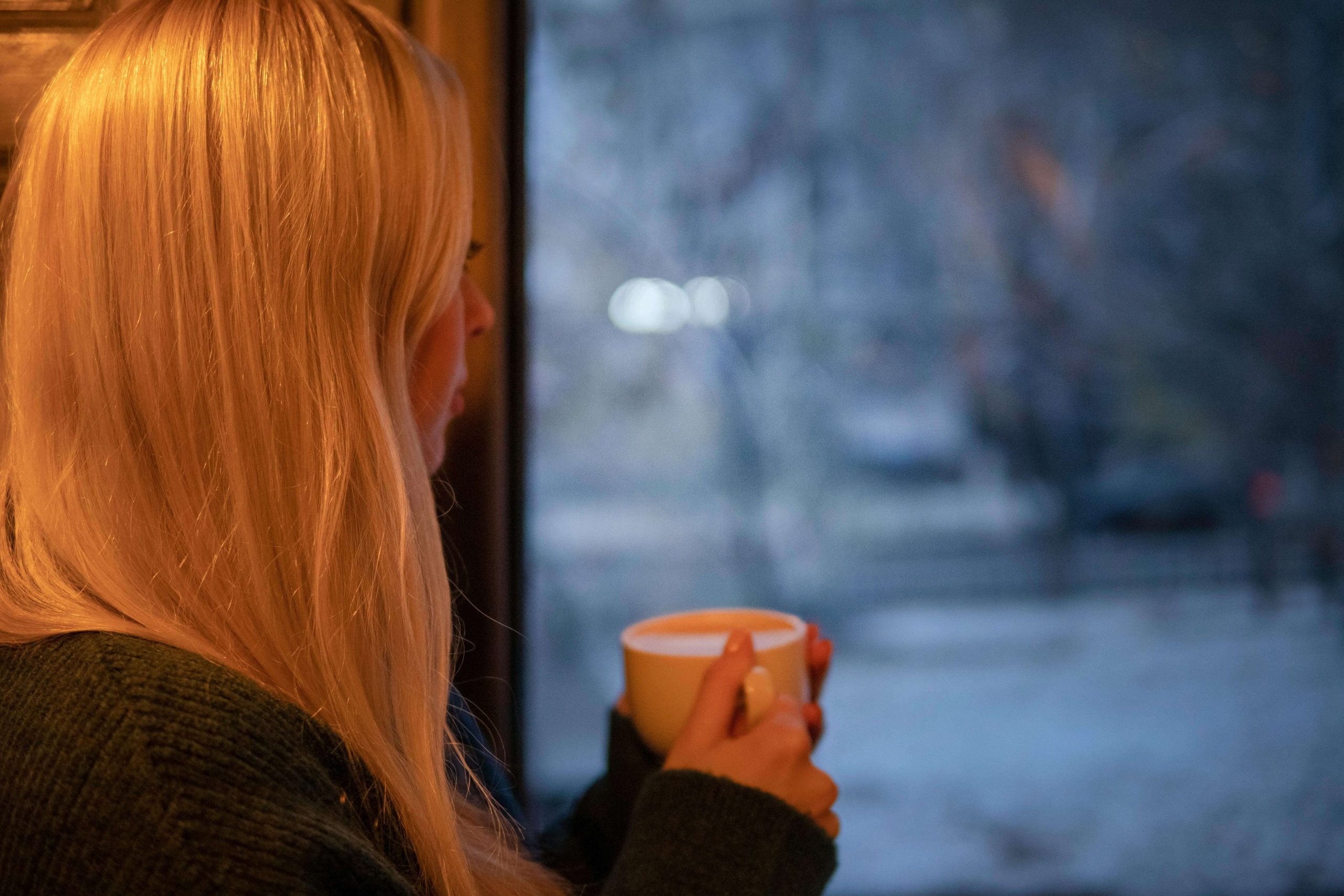 Person holding a mug while looking out a frosty window, capturing the isolation of SAD and the importance of behavioral health in Tempe, AZ.