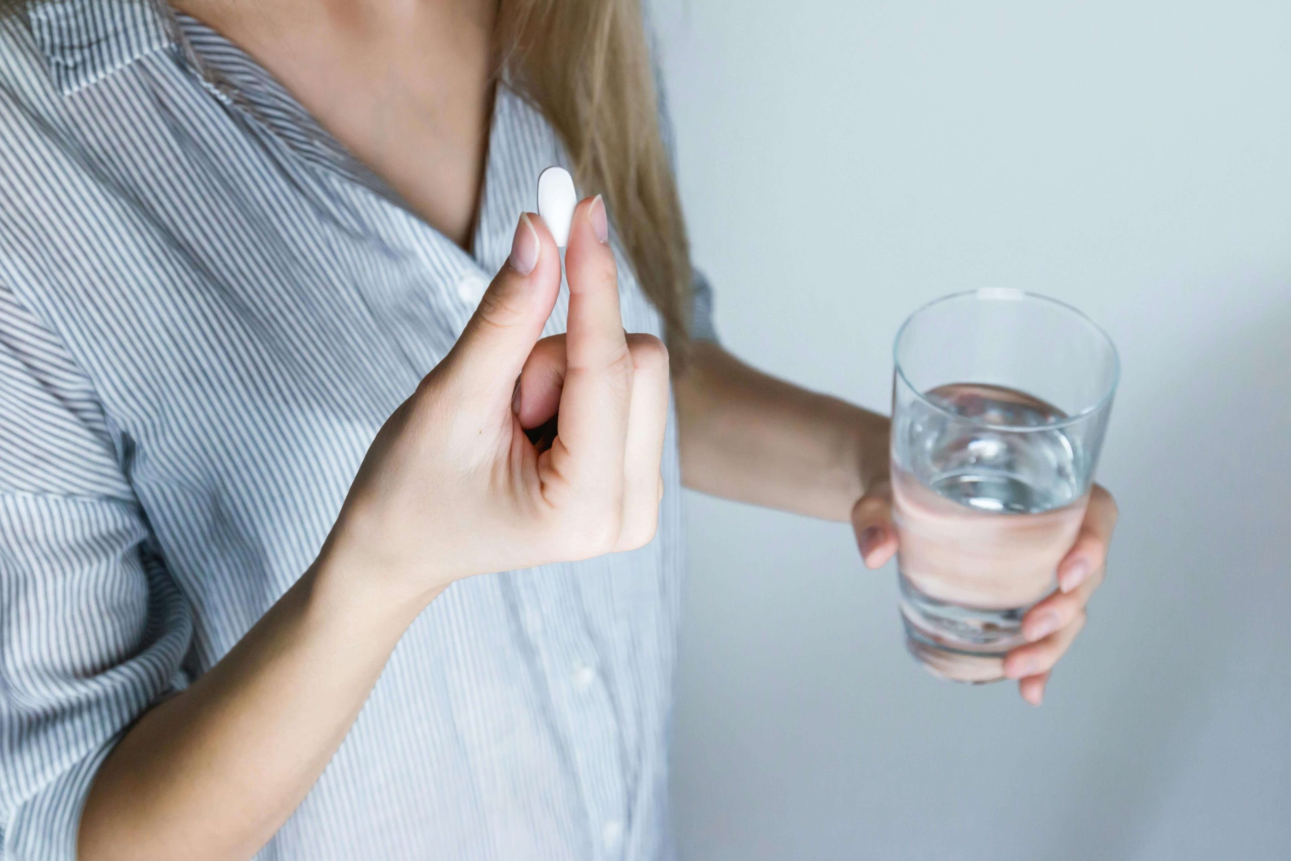A close-up of a woman holding a white ADHD medication tablet and a glass of water, representing the personal routine involved in medication management in Tempe, AZ.