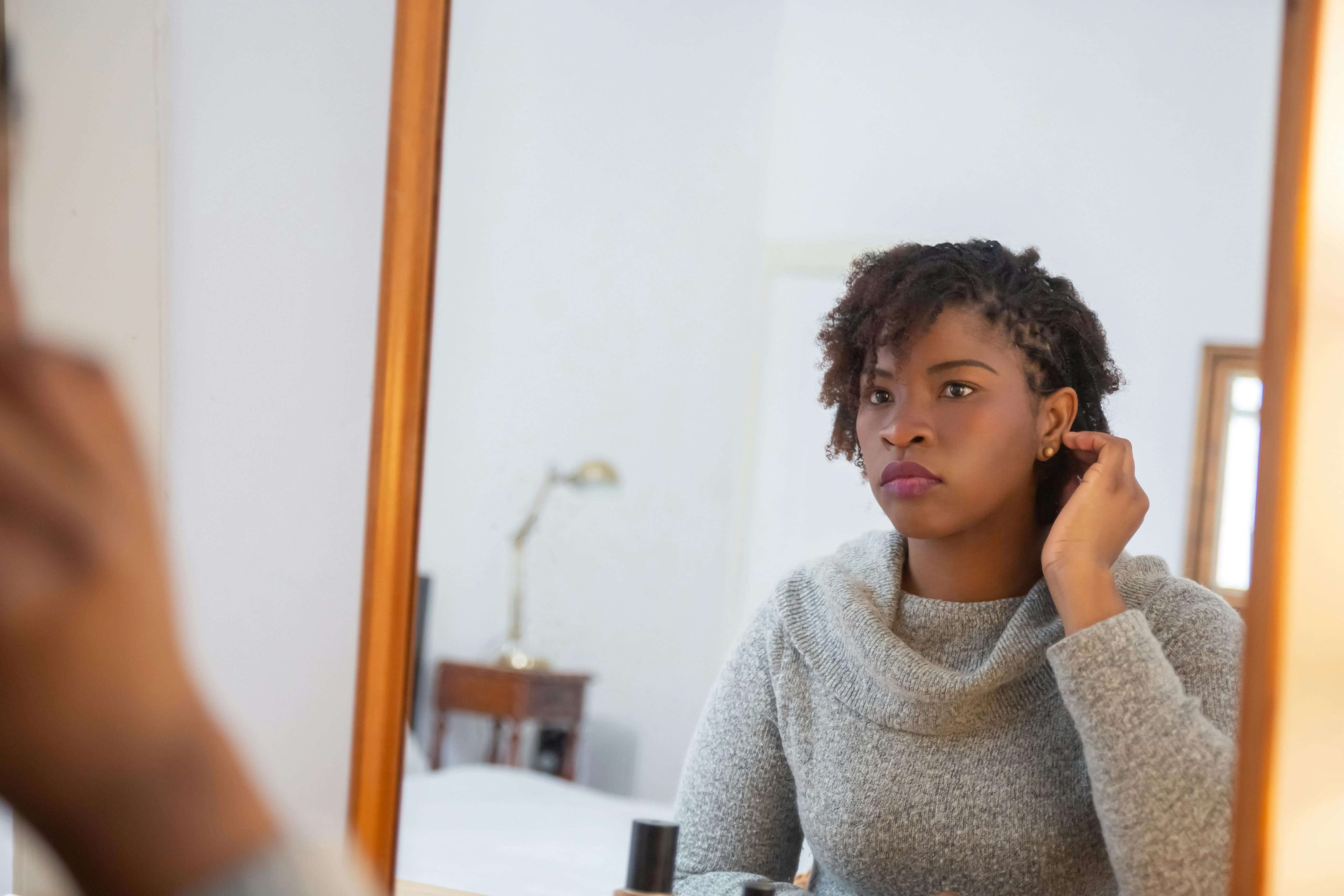 Young woman adjusting her earring in the mirror, her reflection thoughtful, symbolizing inner struggles that may not be visible — a reminder of the importance of compassionate psychiatric care in Tempe, AZ.
