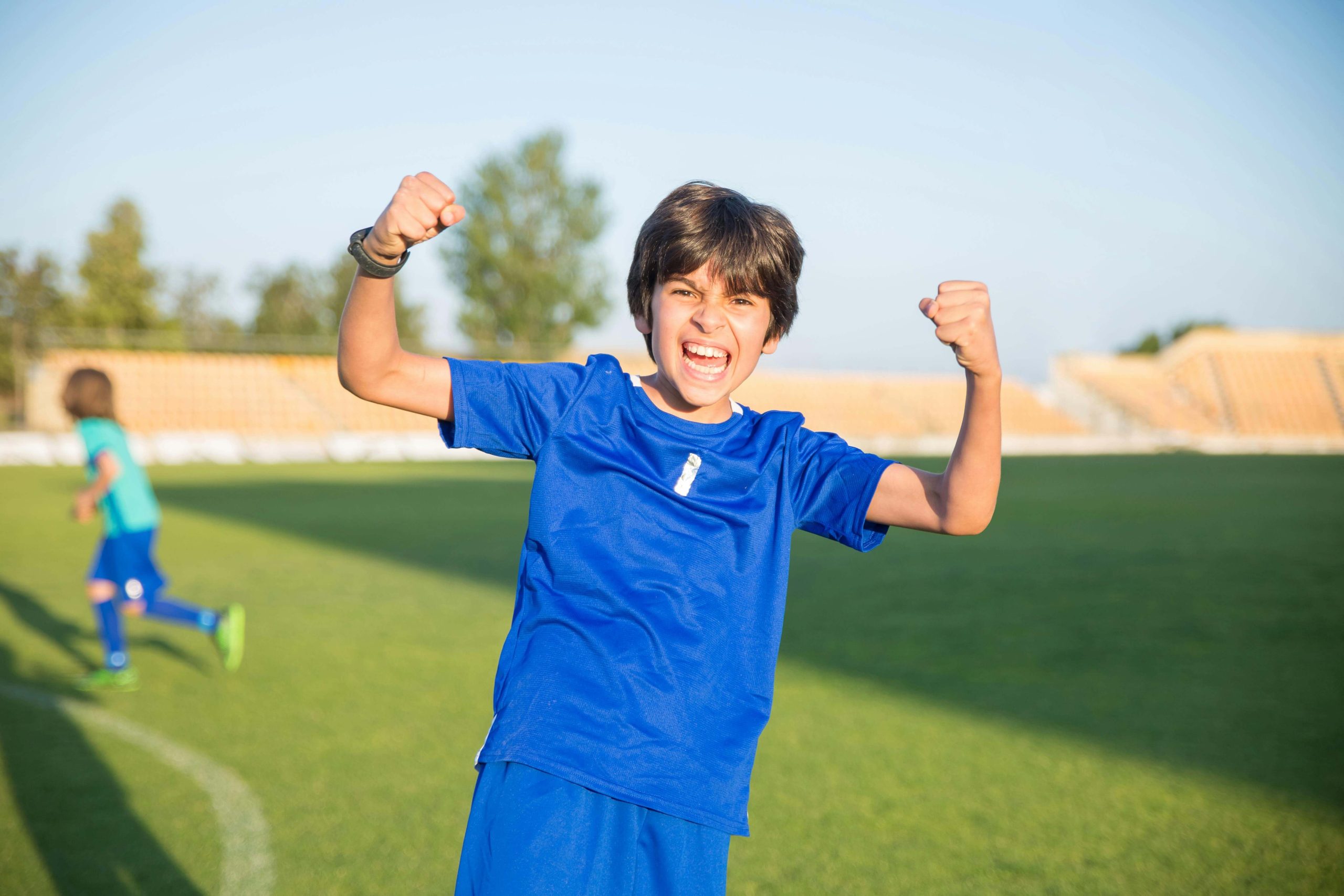 A young boy in a bright blue jersey smiles and pumps his fists in victory on a soccer field, capturing the confidence and focus that can flourish with ADHD support and medication management in Tempe, AZ.