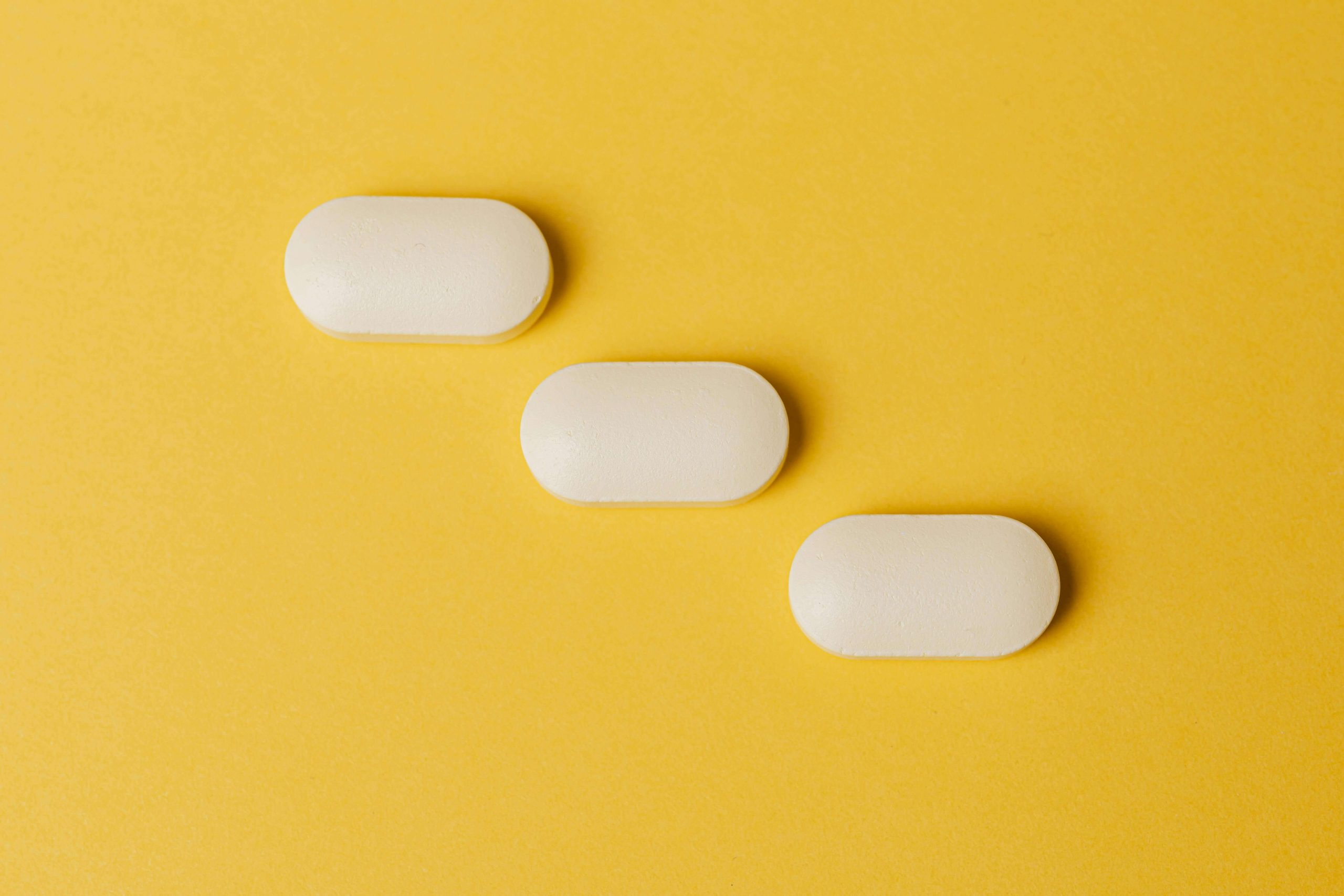 Three white tablets on a yellow background, symbolizing the medication component of mental health treatment in Tempe, AZ.