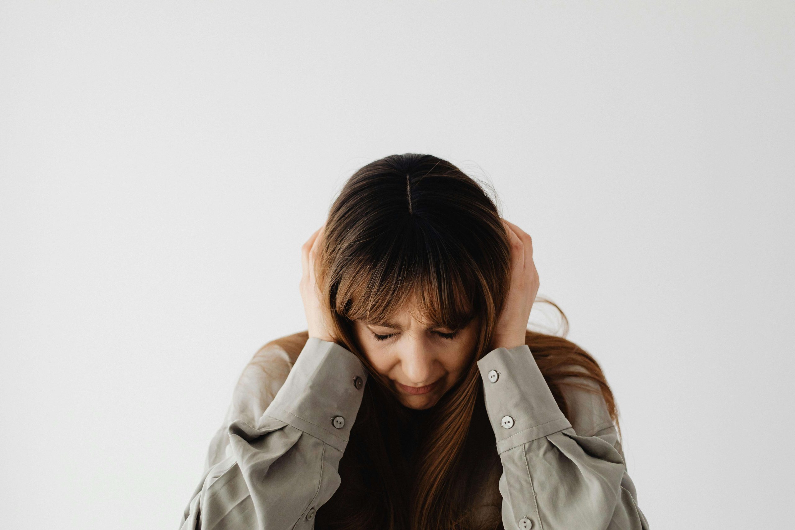 Woman with long hair covering her ears and looking down in emotional pain, representing the challenges of untreated anxiety and depression before seeing a psychiatrist in Tempe, AZ.
