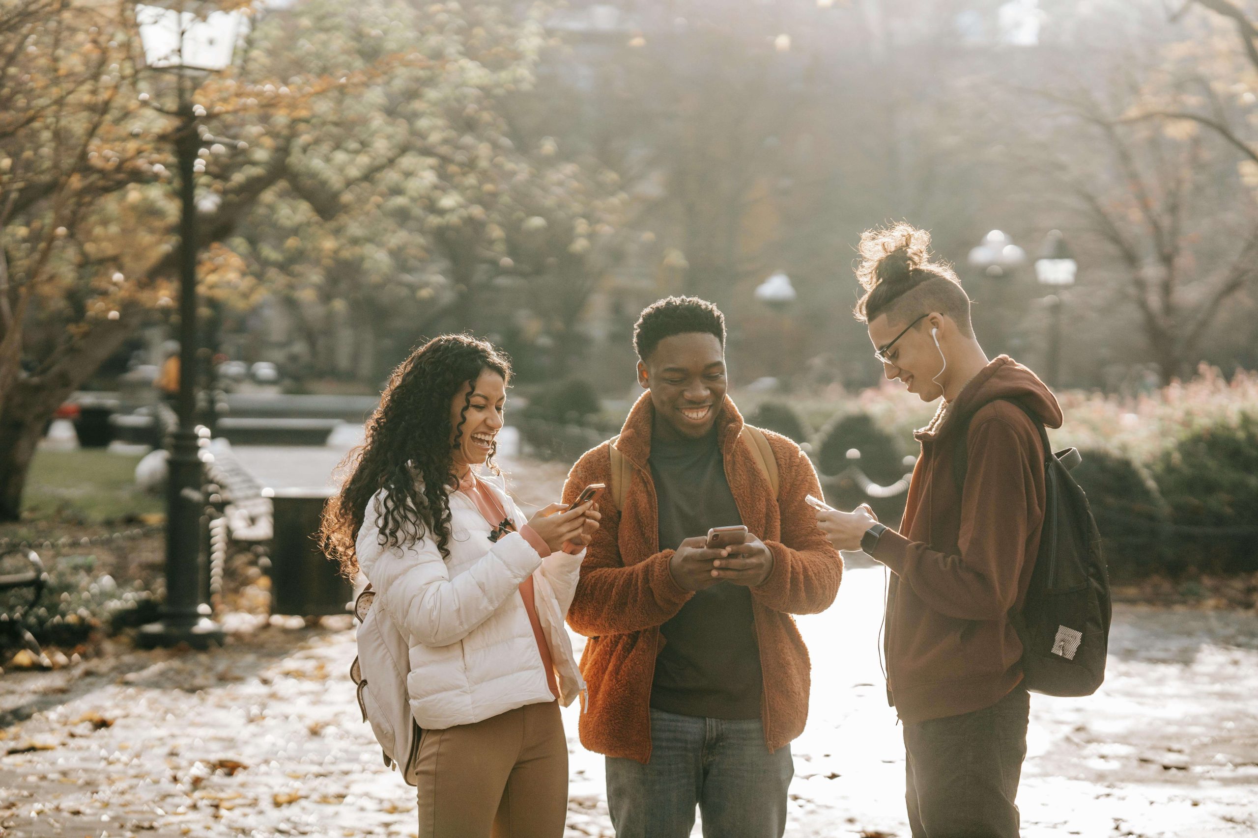 Three young adults smiling and looking at their phones in a sunlit park, symbolizing improved mood and connection after seeking support from a psychiatrist in Tempe, AZ.