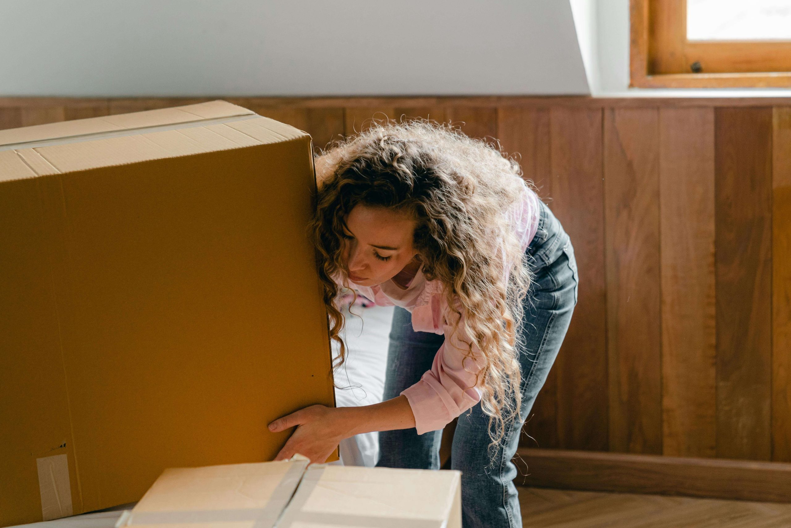 A woman leans forward to lift a heavy box, symbolizing the daily struggles that can feel overwhelming without effective medication management in Tempe, AZ.