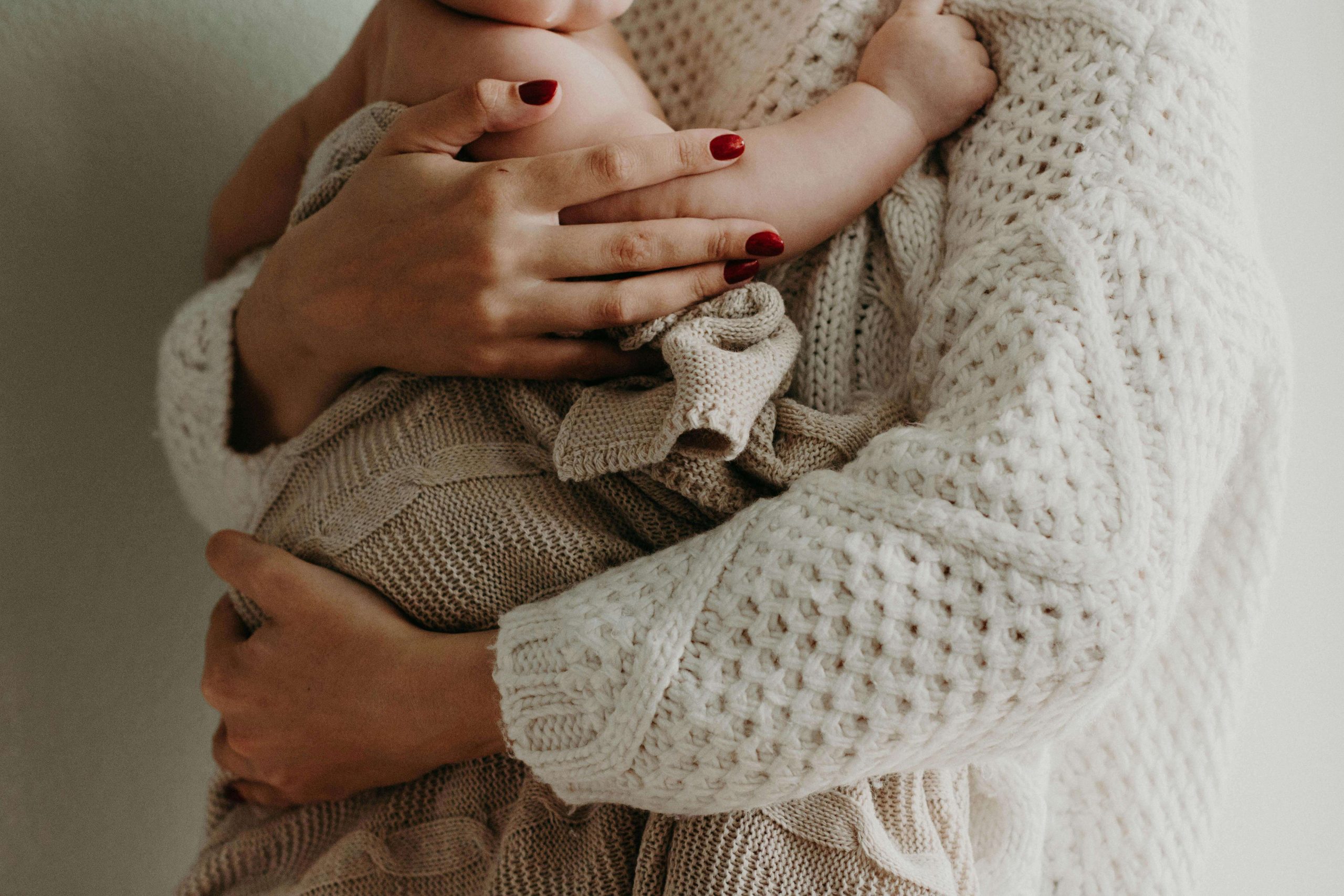 Close-up of a mother in a knitted sweater embracing her baby, highlighting the need for compassionate care and psychiatry in Tempe, AZ during postpartum recovery.