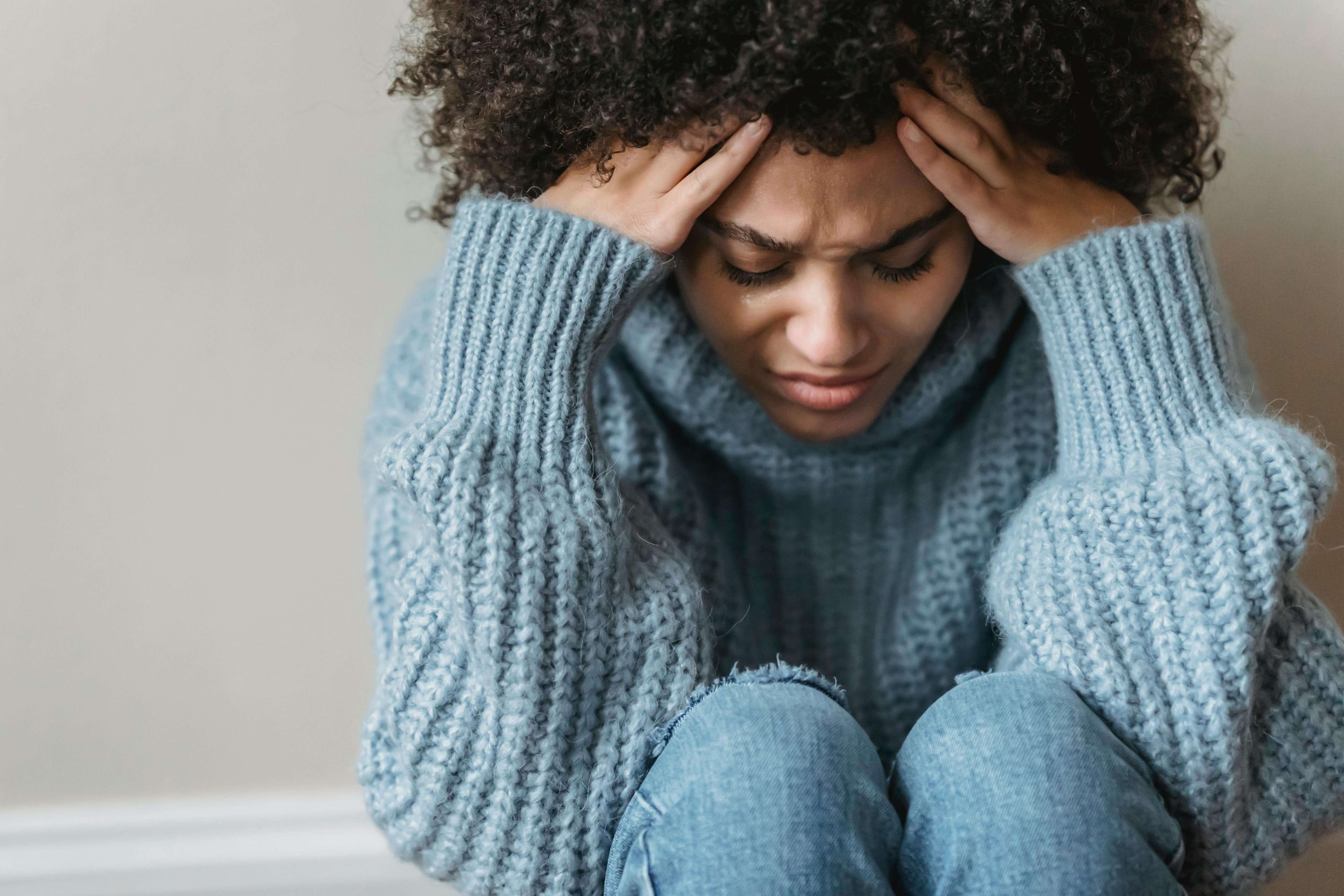 A young woman in a blue sweater holding her head with both hands, expressing emotional distress often addressed in bipolar disorder therapy in Tempe AZ.
