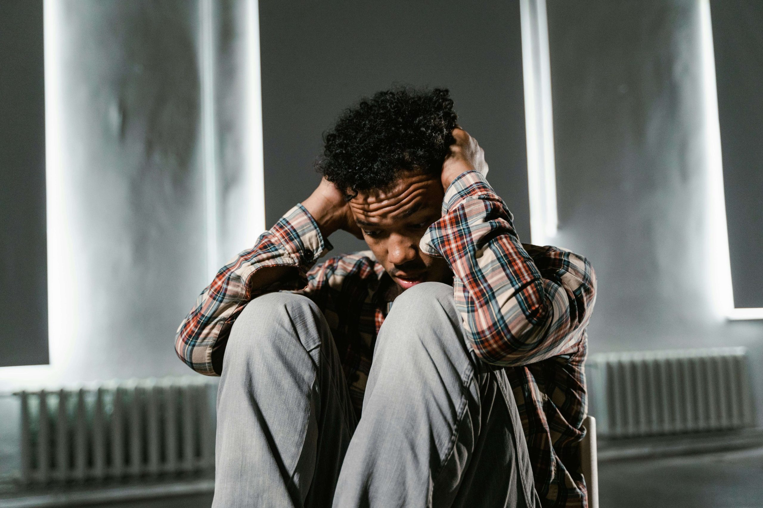 Man sitting on the floor with hands on his head, appearing overwhelmed, highlighting the symptoms of anxiety and depression that may be eased with help from a psychiatrist in Tempe, AZ.