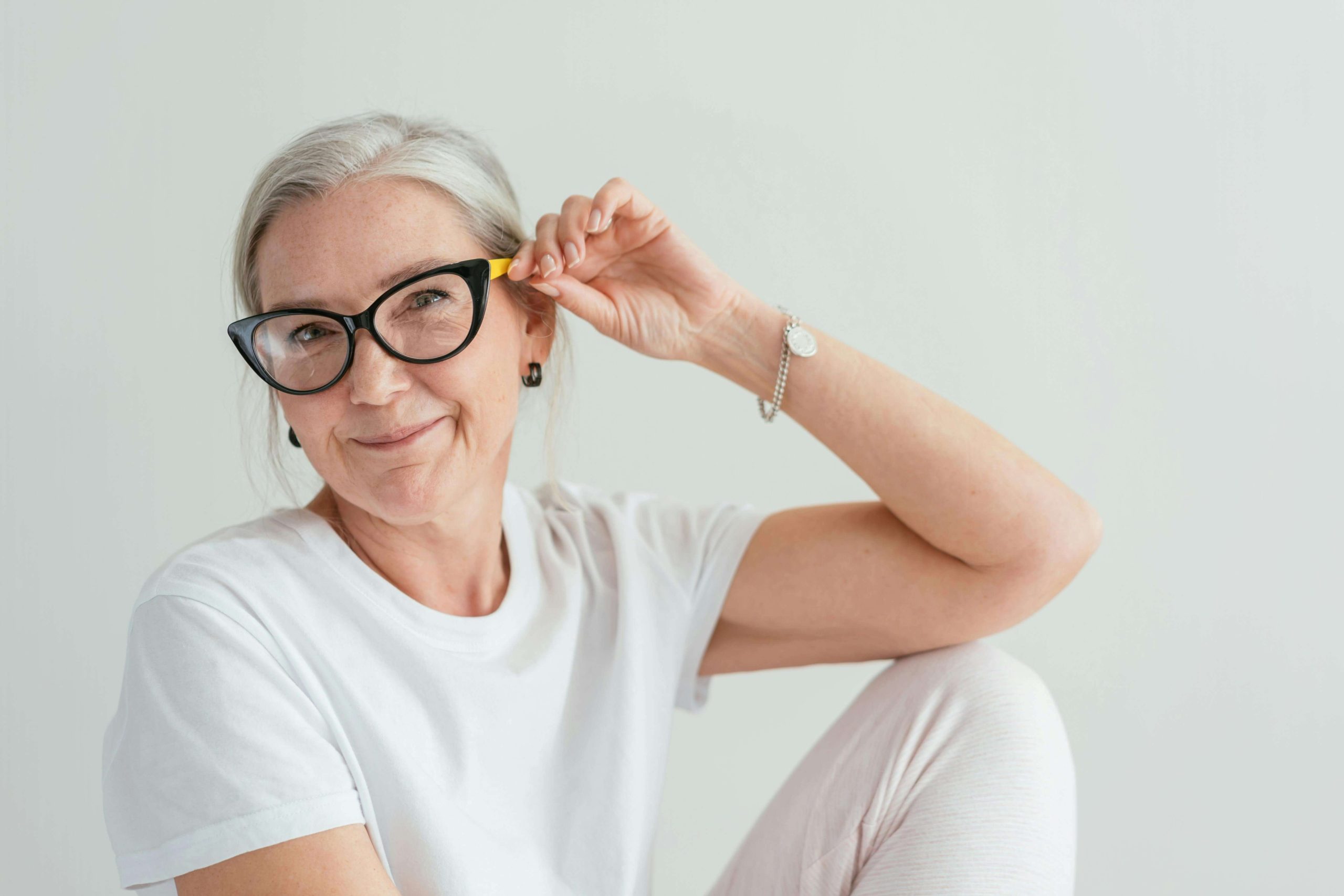 Older Woman - psychiatric care tempe - psychiatry tempe az - medication management tempe az - phx - phoenix - gilbert - scottsdale - mesa - arizona Older woman in glasses smiling gently in a bright, minimal space, representing resilience and self-acceptance supported through psychiatric care in Tempe, AZ.