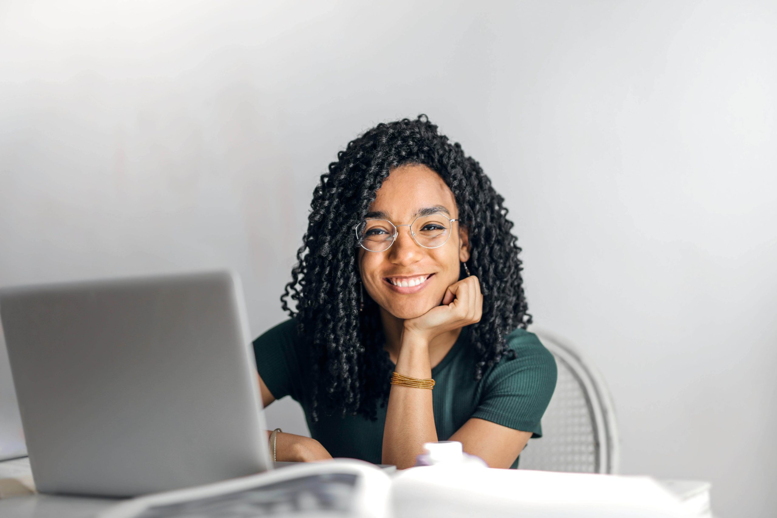 A smiling woman with glasses sits confidently at a laptop, representing the empowerment and stability many adults find through effective psychiatric care in Tempe, AZ, for managing ADHD.