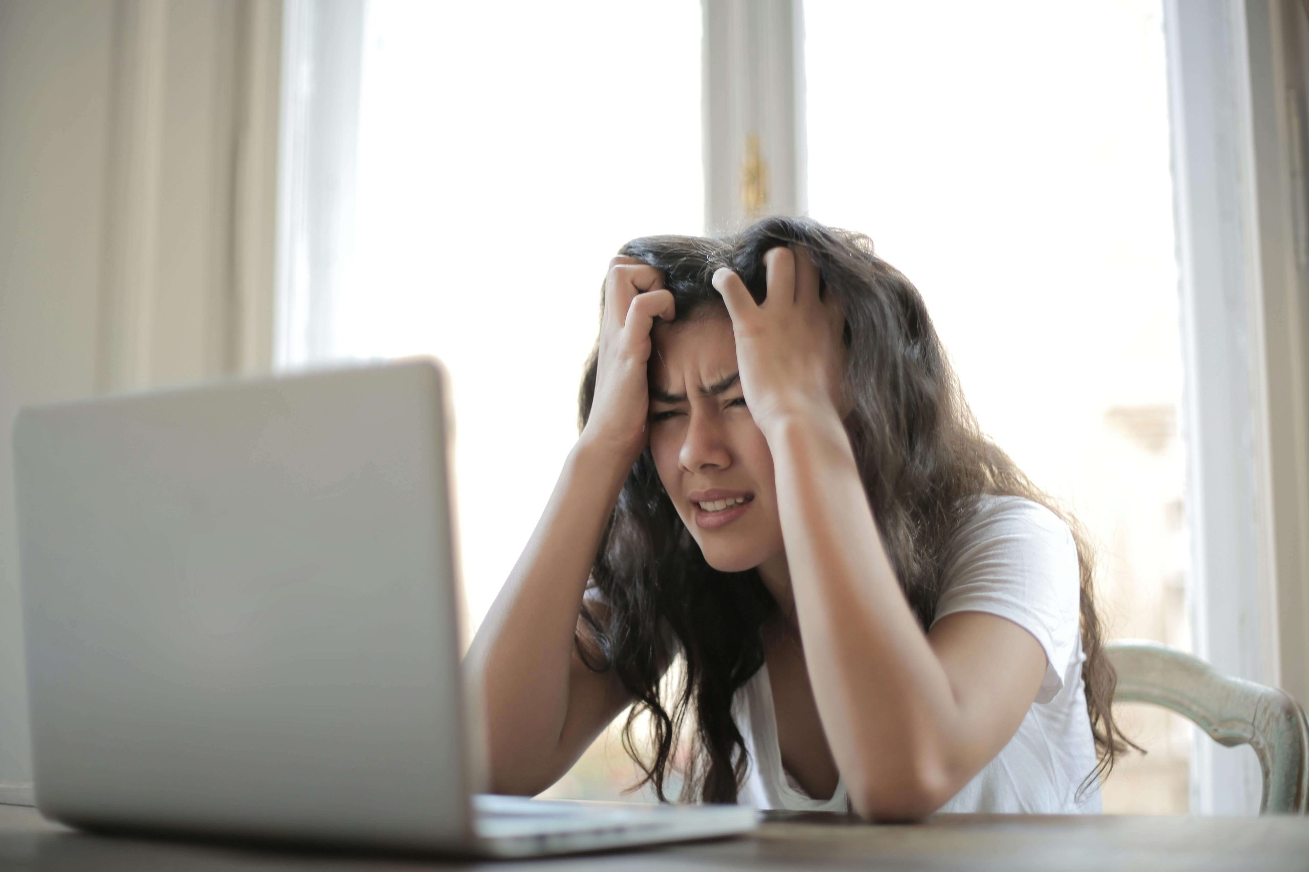 Stressed woman gripping her head while looking at laptop, reflecting the everyday struggles with anxiety and the importance of psychiatric care in Tempe, AZ.