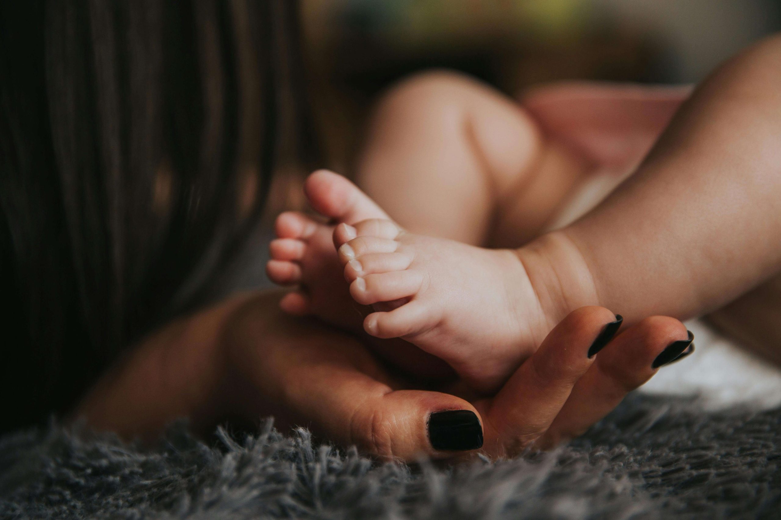 Close-up of a mother gently holding her newborn’s tiny feet, symbolizing the tender moments of early motherhood and the emotional challenges supported by psychiatry in Tempe, AZ.