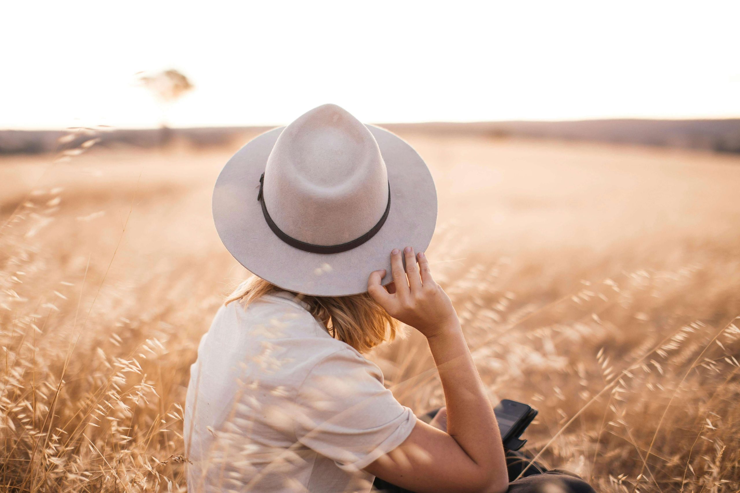 A person wearing a wide-brimmed hat sitting in a golden field, reflecting on life, representing moments of calm and self-reflection encouraged during bipolar disorder therapy in Tempe AZ.