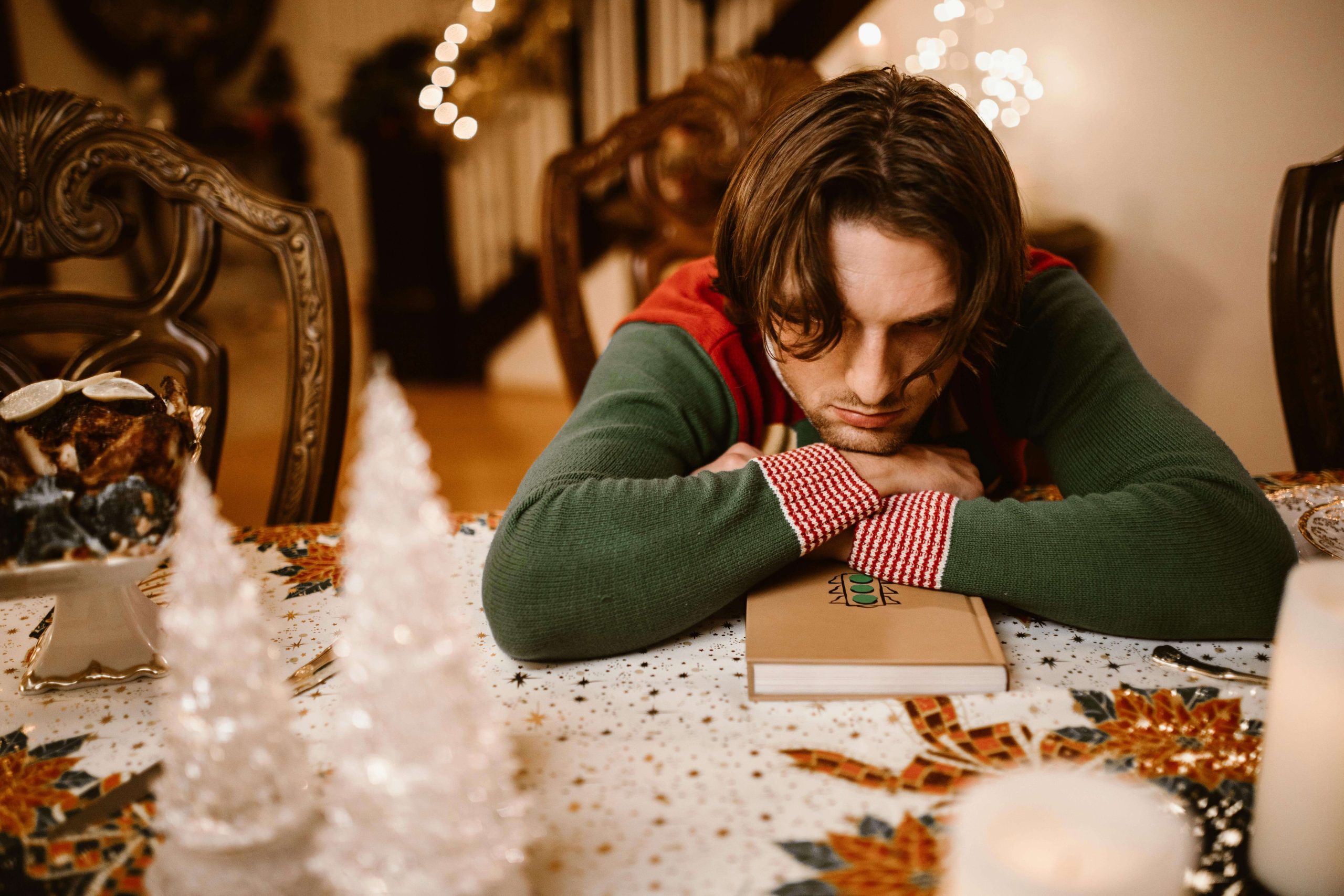 Man in a festive sweater resting his head on his arms at a holiday table, showing burnout and seasonal triggers addressed by a psychiatrist for stress in Tempe, AZ.