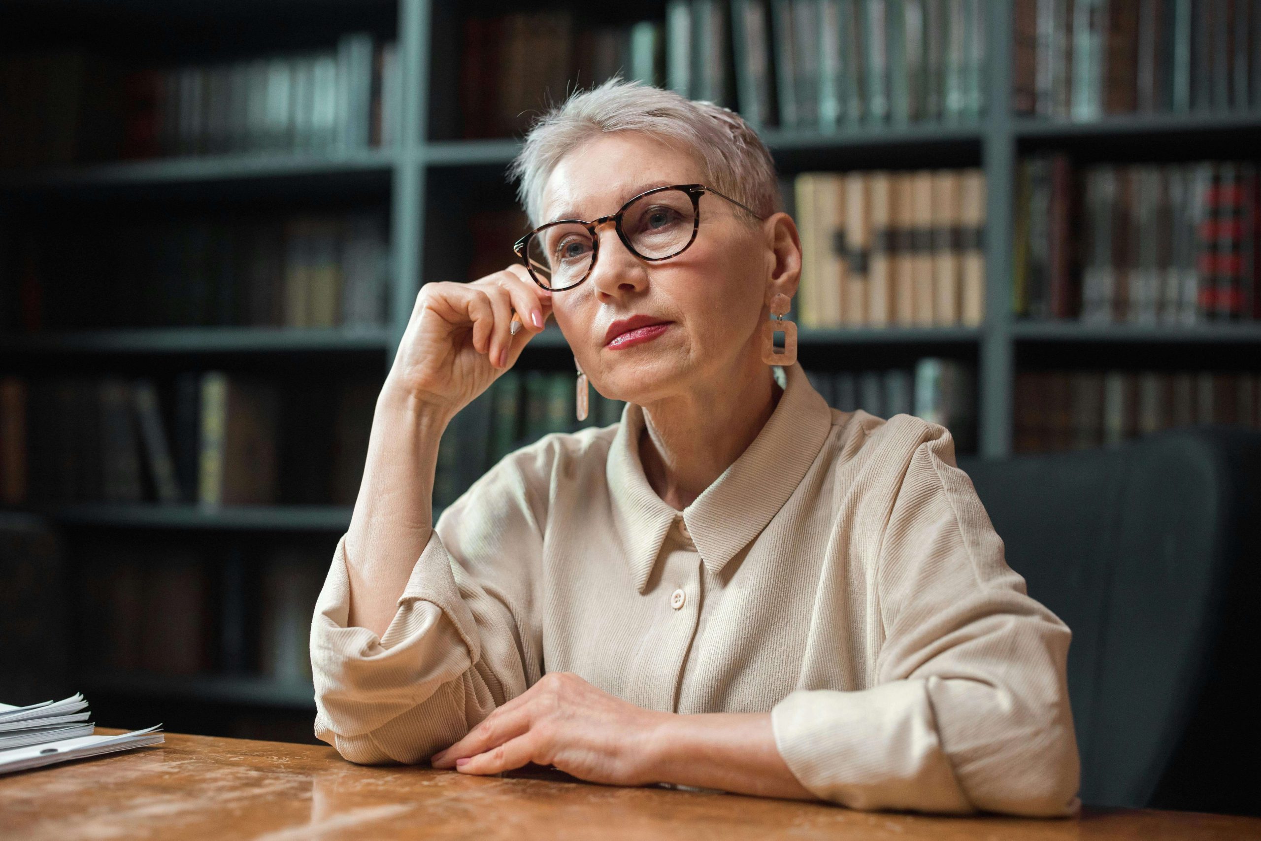 Mature woman sitting thoughtfully in a library, representing reflection and healing through psychiatry in Tempe AZ for cannabis-related mood changes.