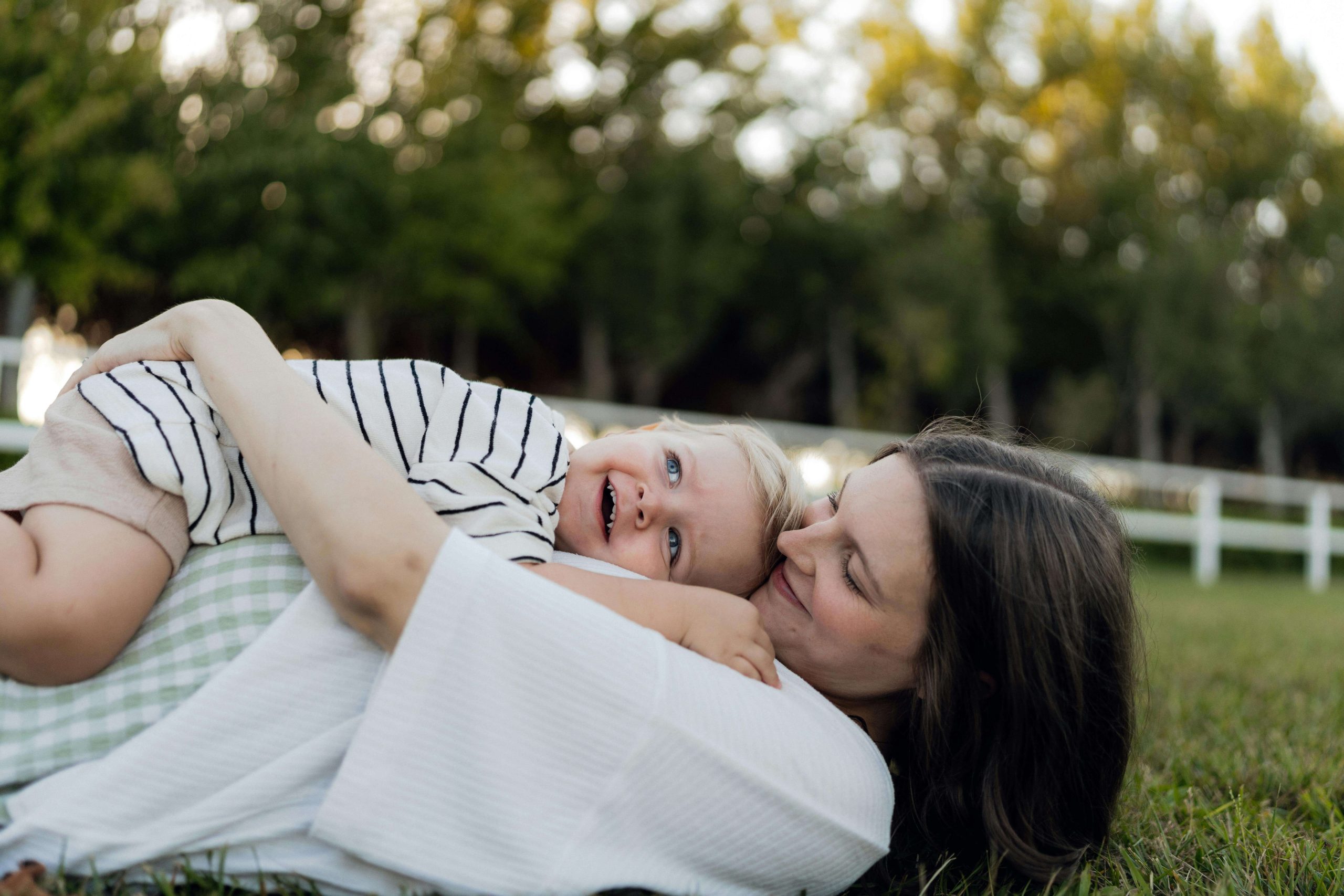 Mother lying in the grass holding her smiling toddler, representing the bond between parent and child and how psychiatry in Tempe, AZ helps mothers navigate postpartum mood changes.