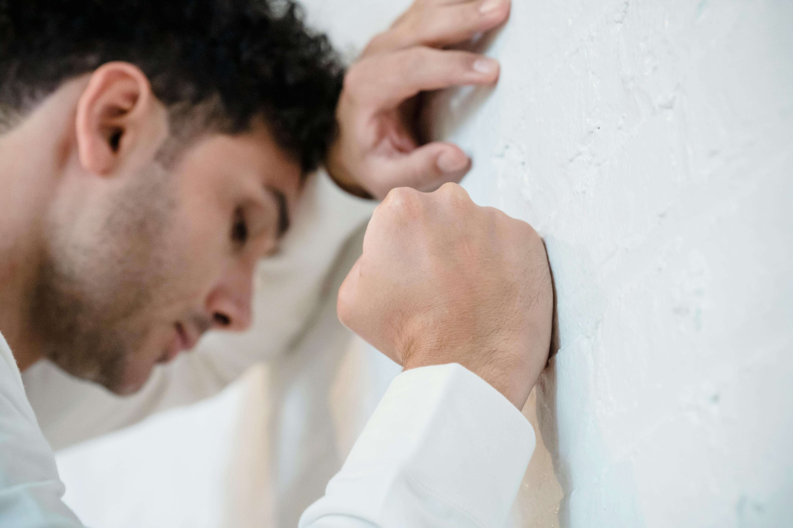 Stressed man leaning against a wall with clenched fist, showing the struggles of anxiety and addiction addressed by a psychiatrist in Tempe, AZ.