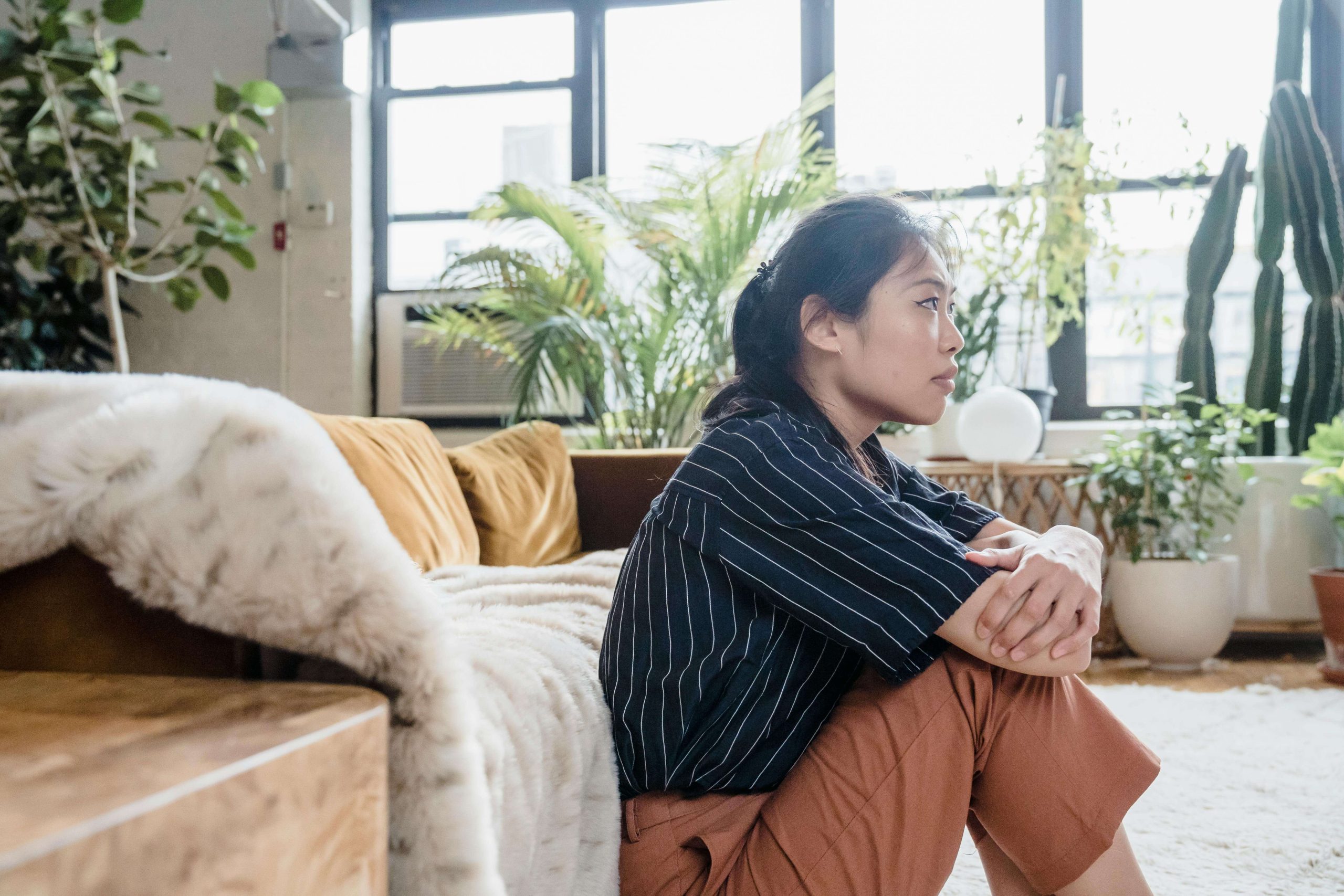Woman sitting thoughtfully in a cozy living room with plants, symbolizing the support behavioral health in Tempe, AZ can provide for seasonal affective disorder.