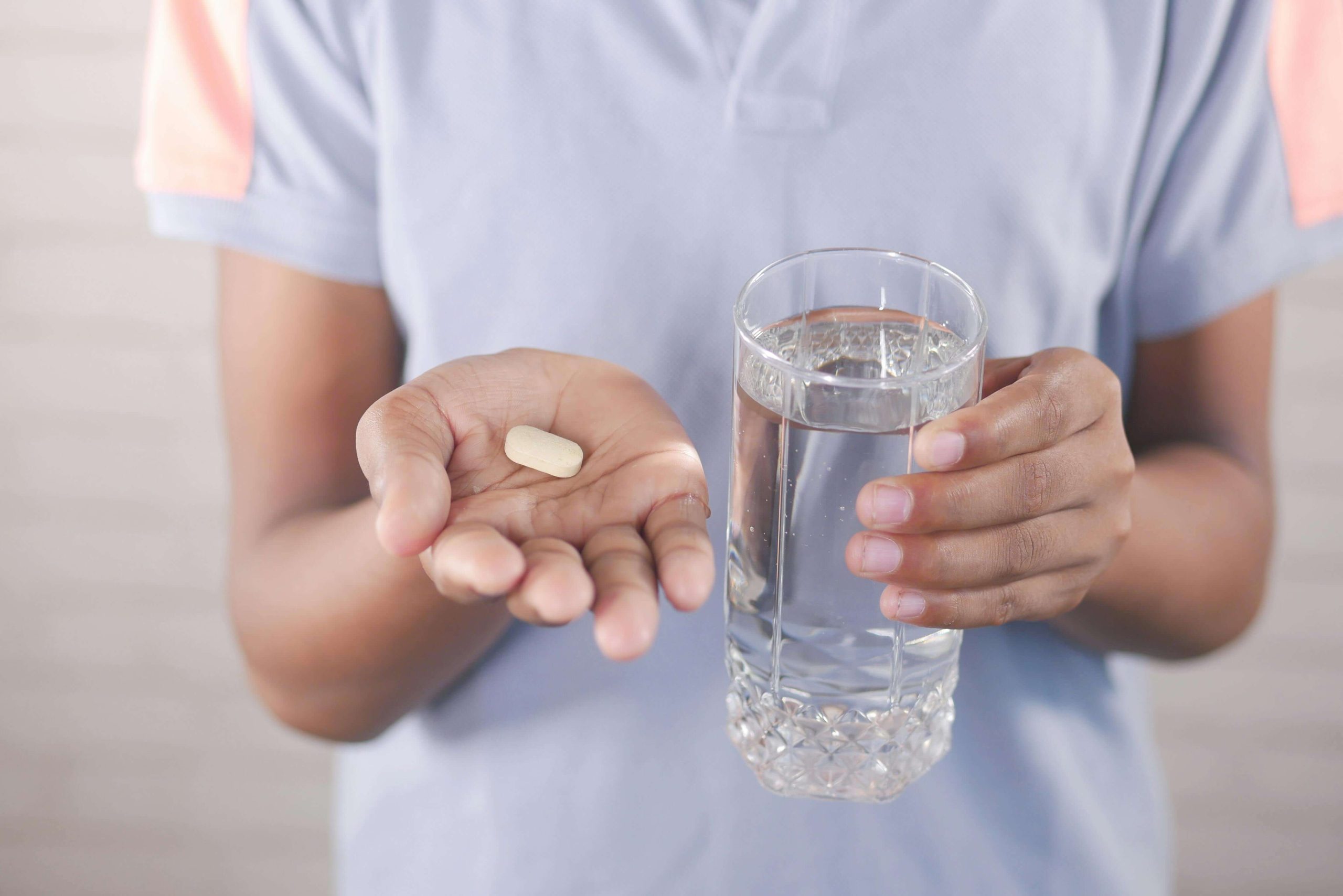 Someone holds a pill in one hand and a glass of water in the other, showing the role of consistent treatment in medication management in Tempe, AZ.