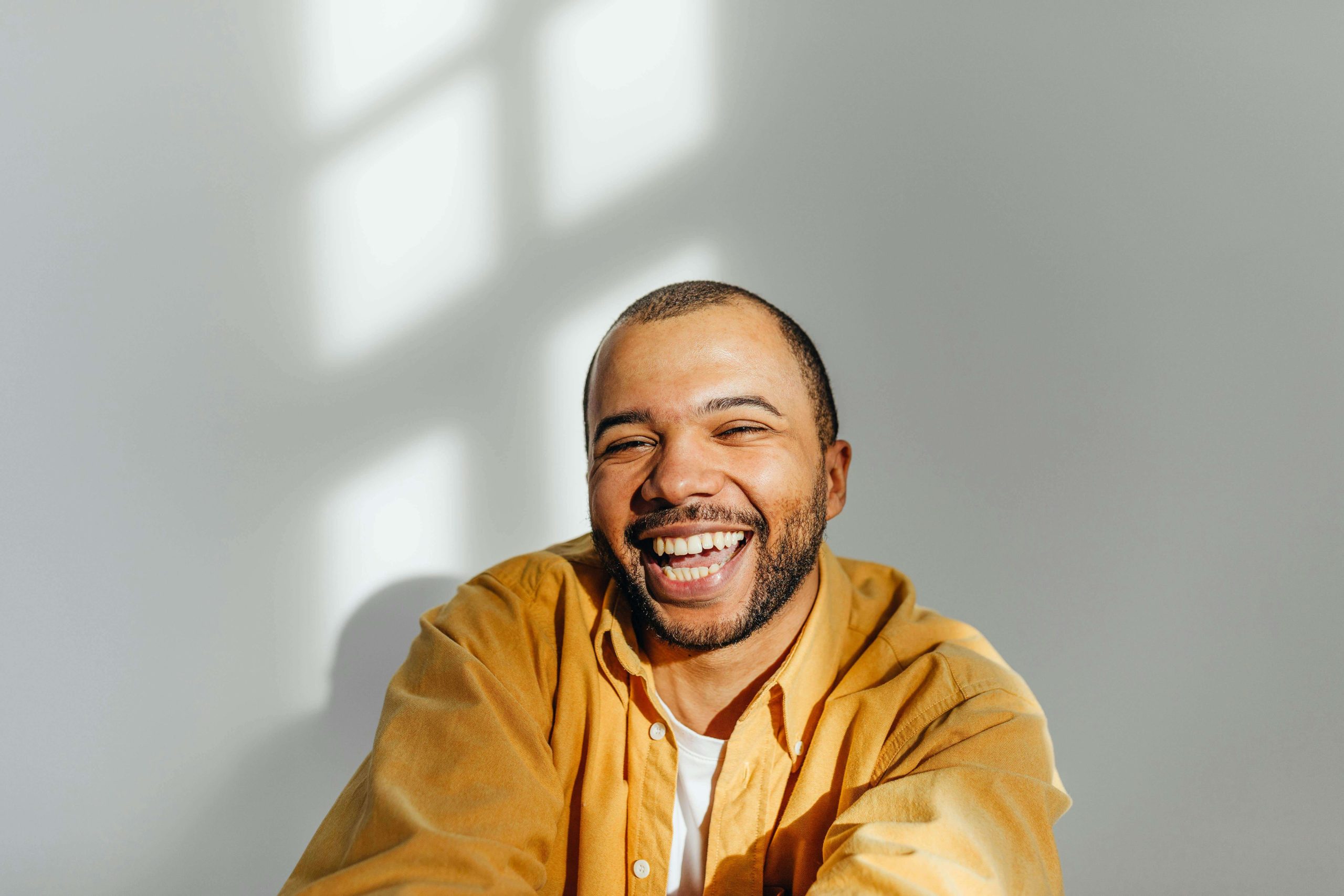 A man in a yellow shirt smiling brightly in natural light, symbolizing positive mental health outcomes from psychiatry in Tempe, AZ.